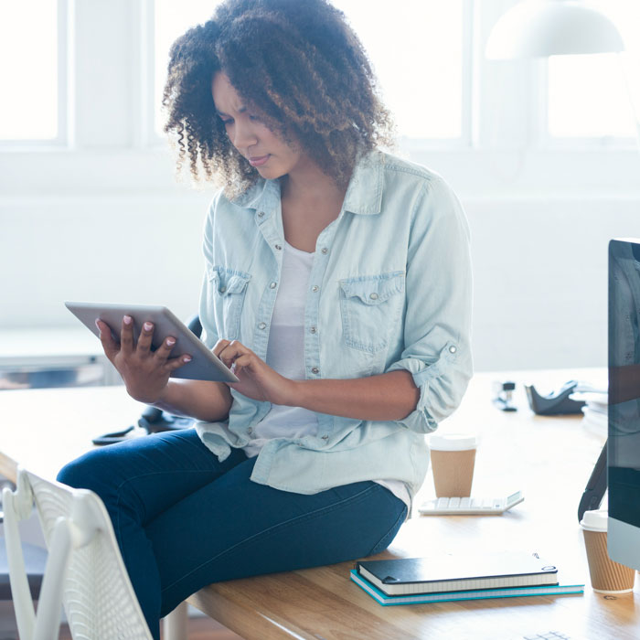A young woman sitting on a desk and using a tablet