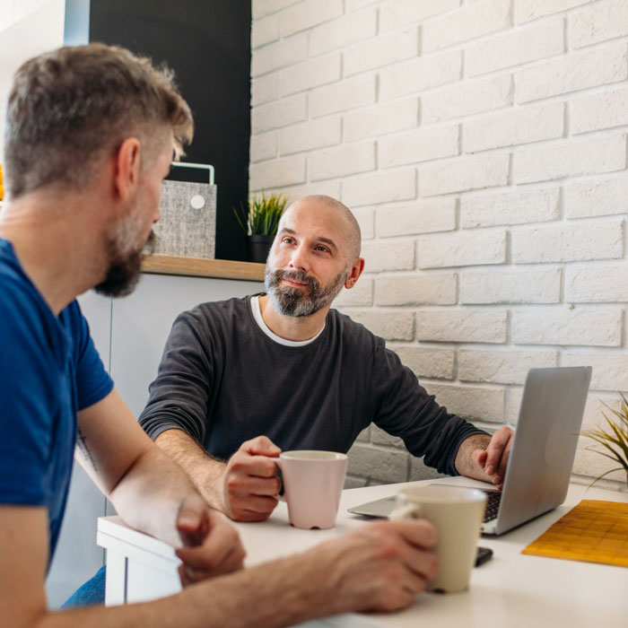 Two seated men talking while using a laptop