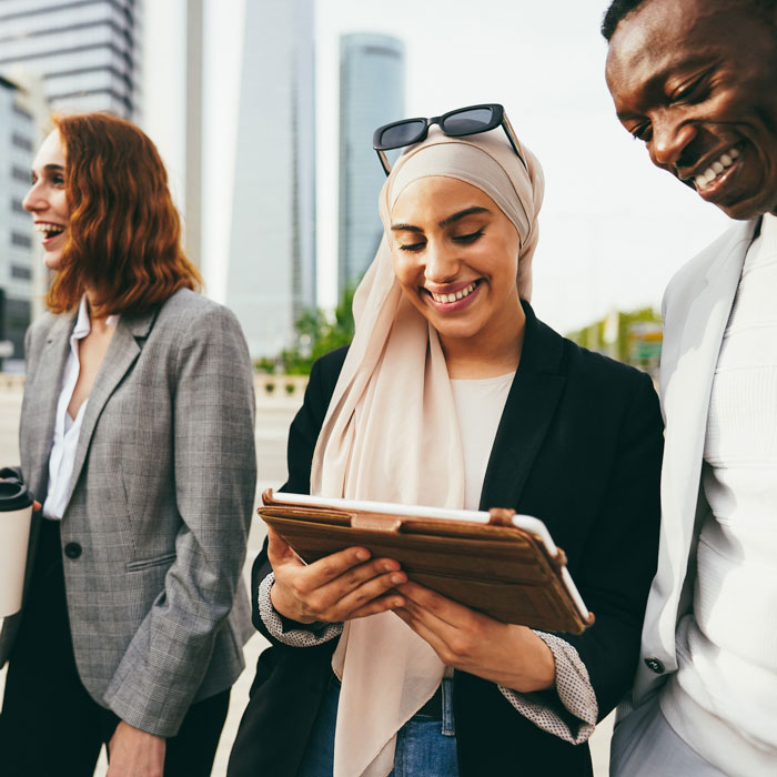 Multiracial business people laughing and smiling outdoors while using a tablet
