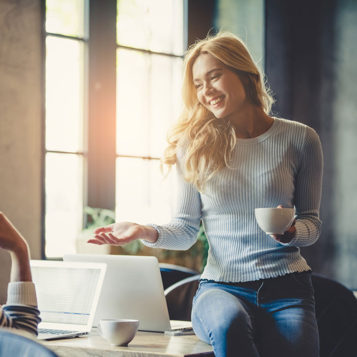 A young woman talking in an office while holding coffee