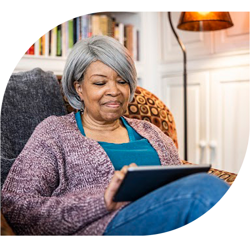 An elderly woman sitting in a chair and looking at a tablet
