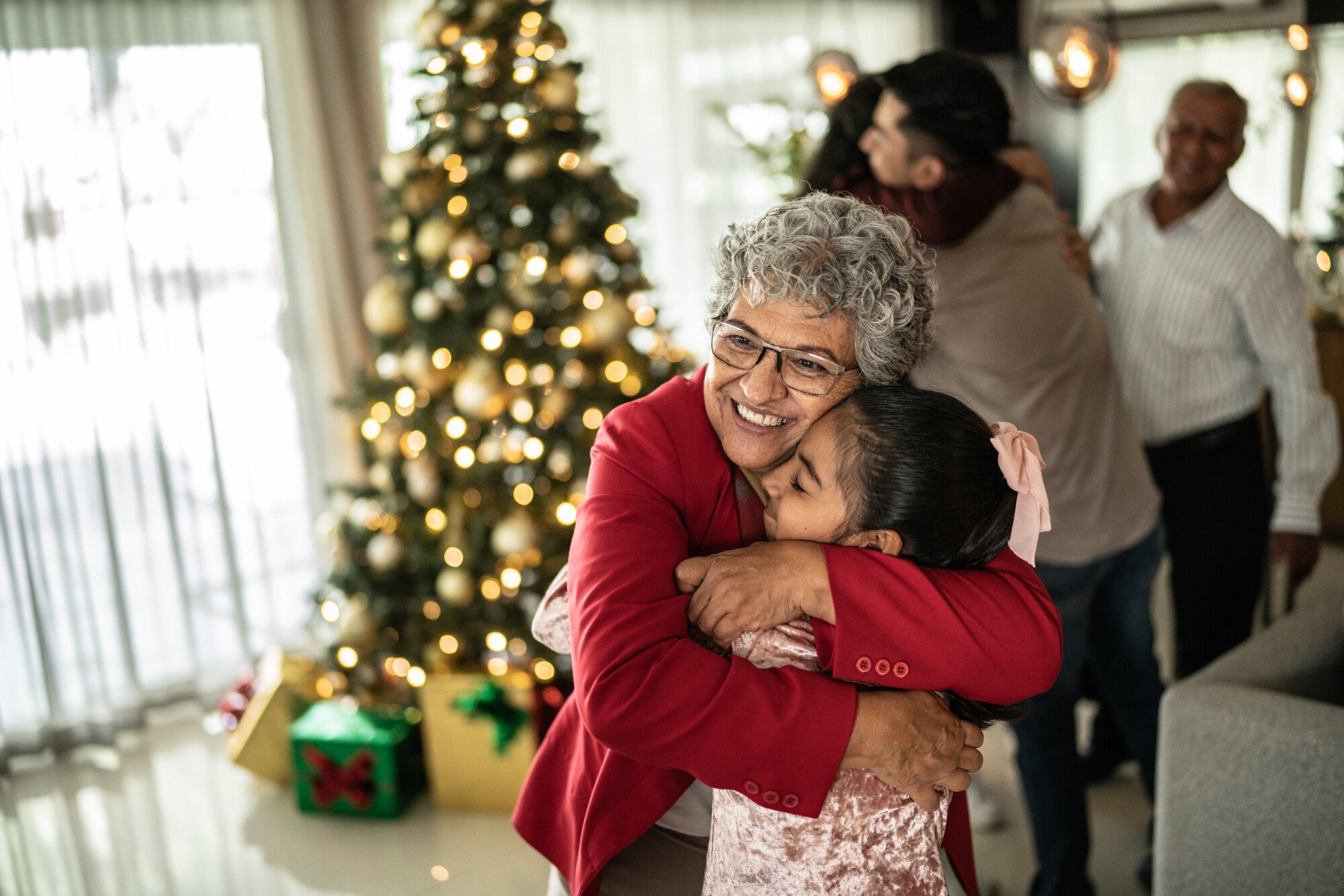 Older woman hugging young girl near a Christmas tree