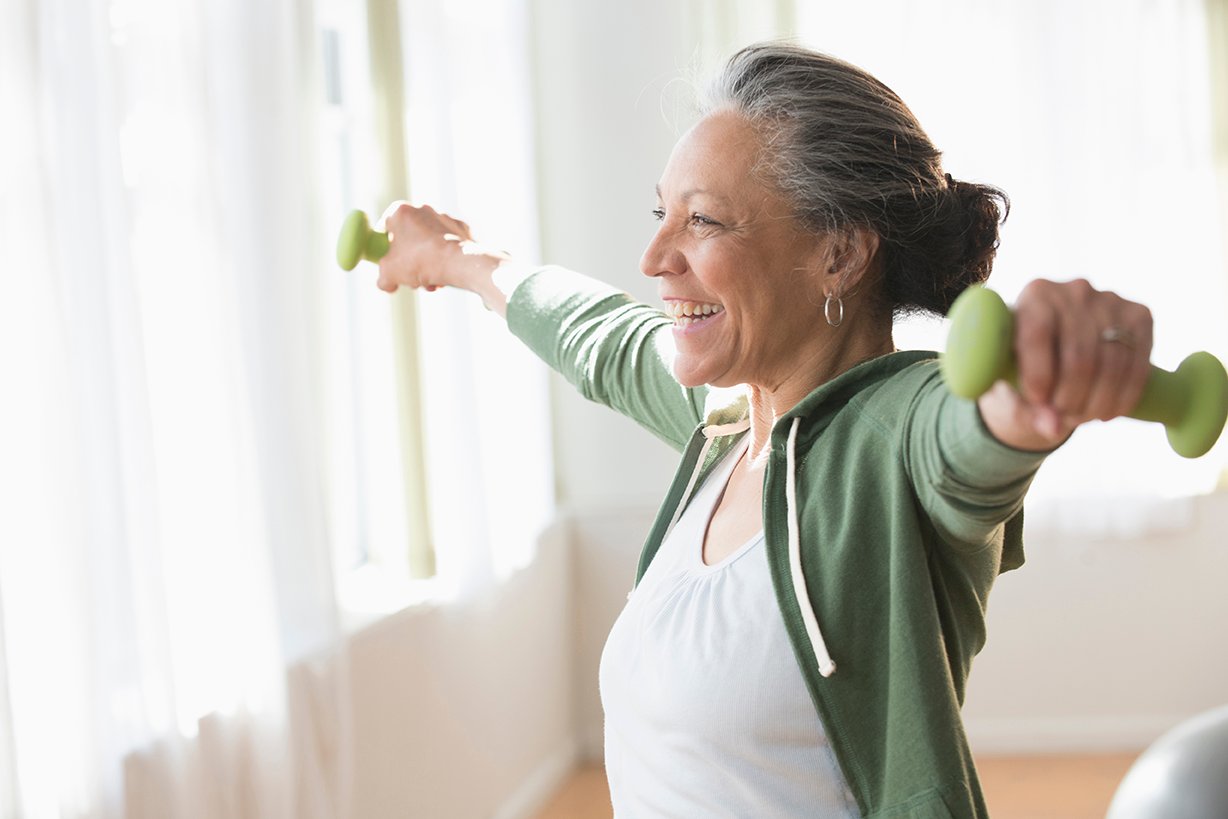A smiling senior woman exercising at home using small, green dumbbells