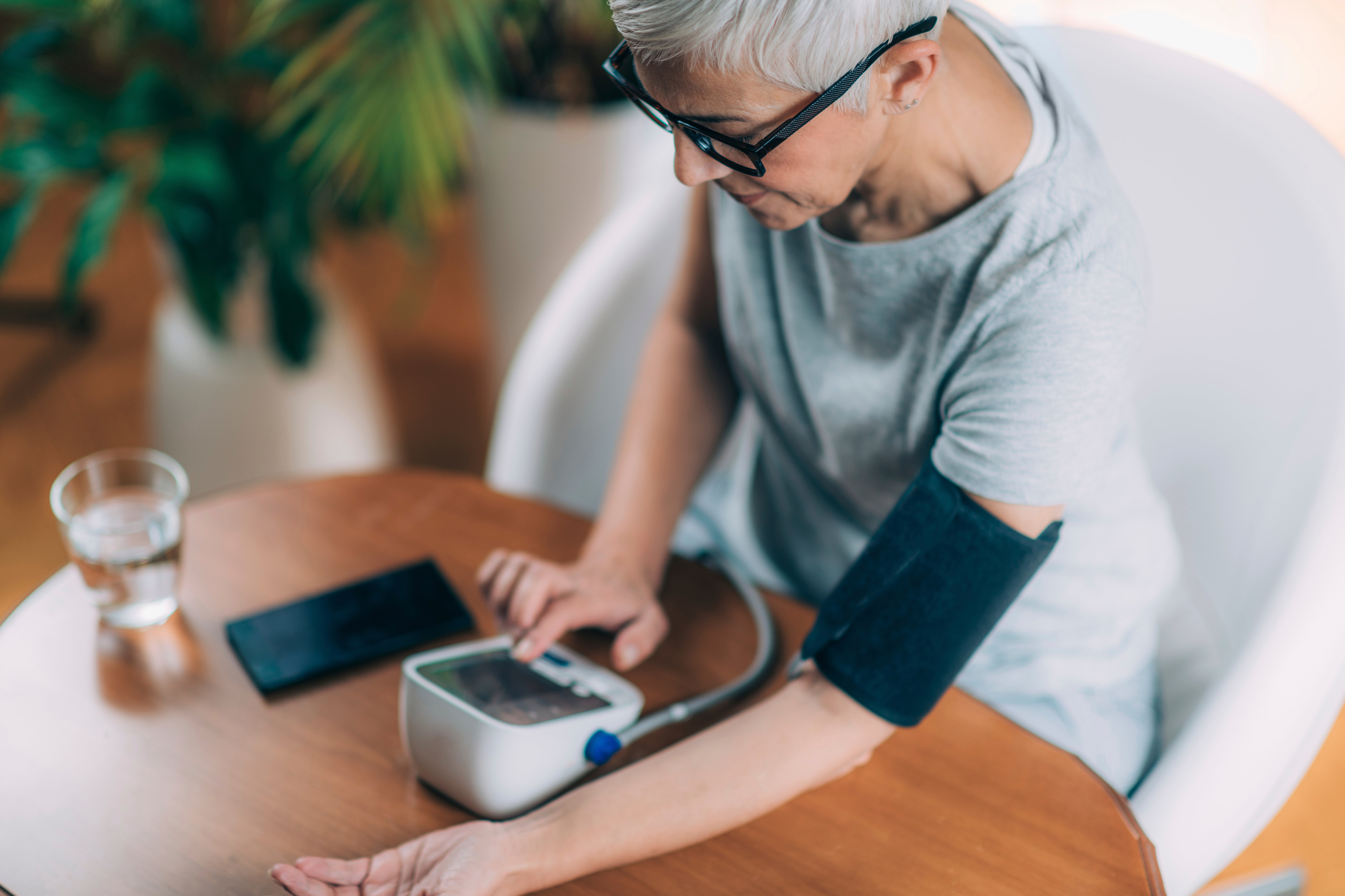 A woman sits at a table, using a digital monitor to check her own blood pressure