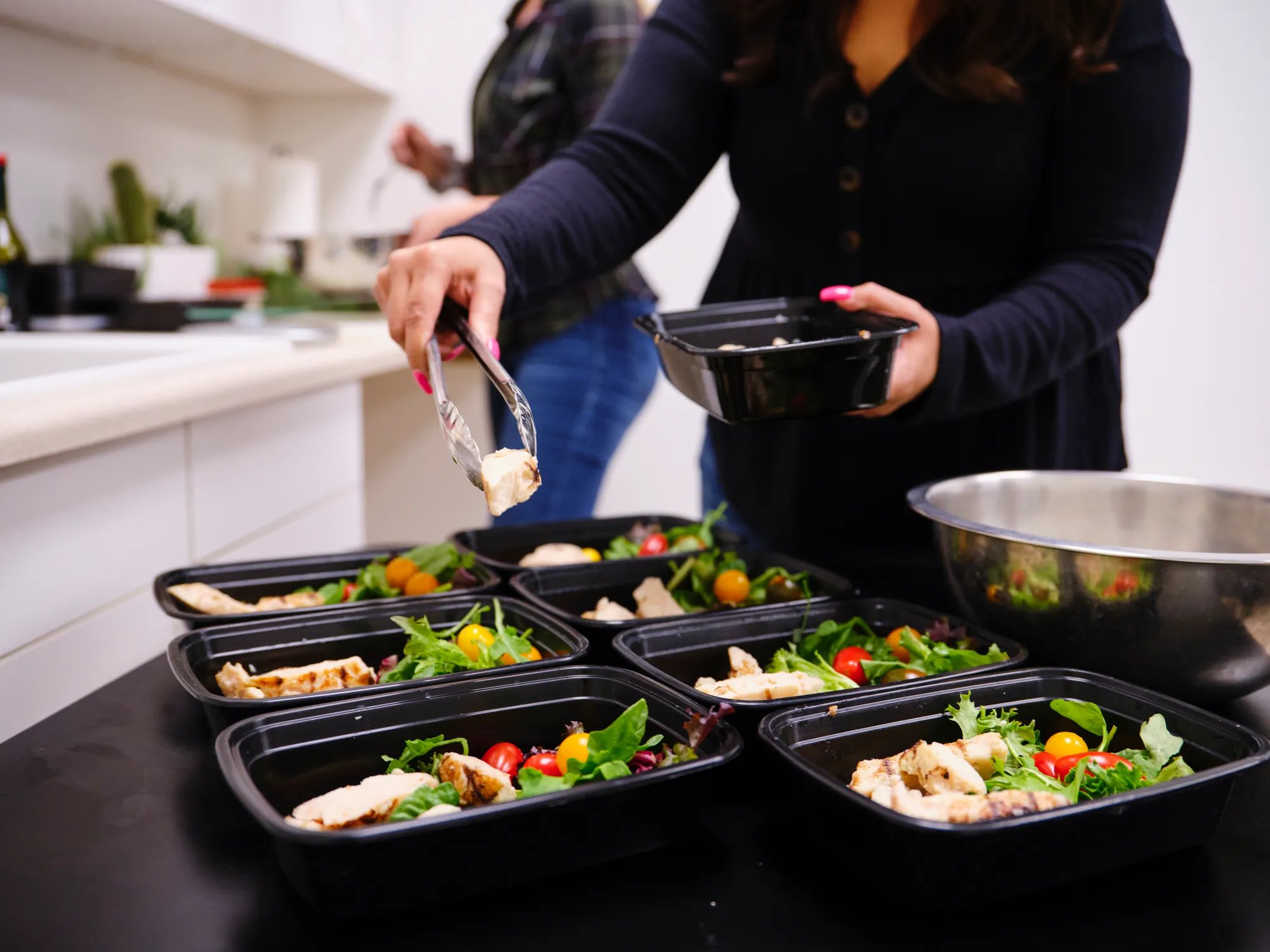 A woman portions out a healthy meal in her kitchen using bento trays