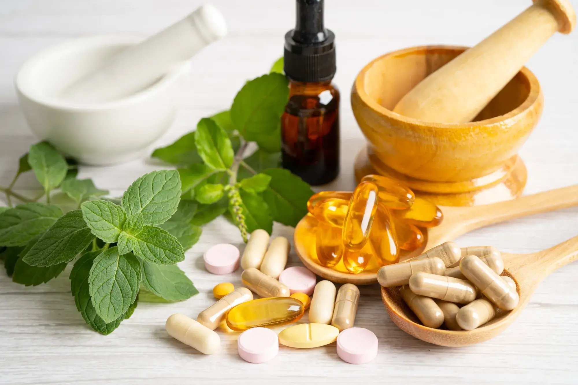 A grouping of alternative medicines, bowls with pestles, organic herbs, and vitamin E and omega 3 fish oil capsules.