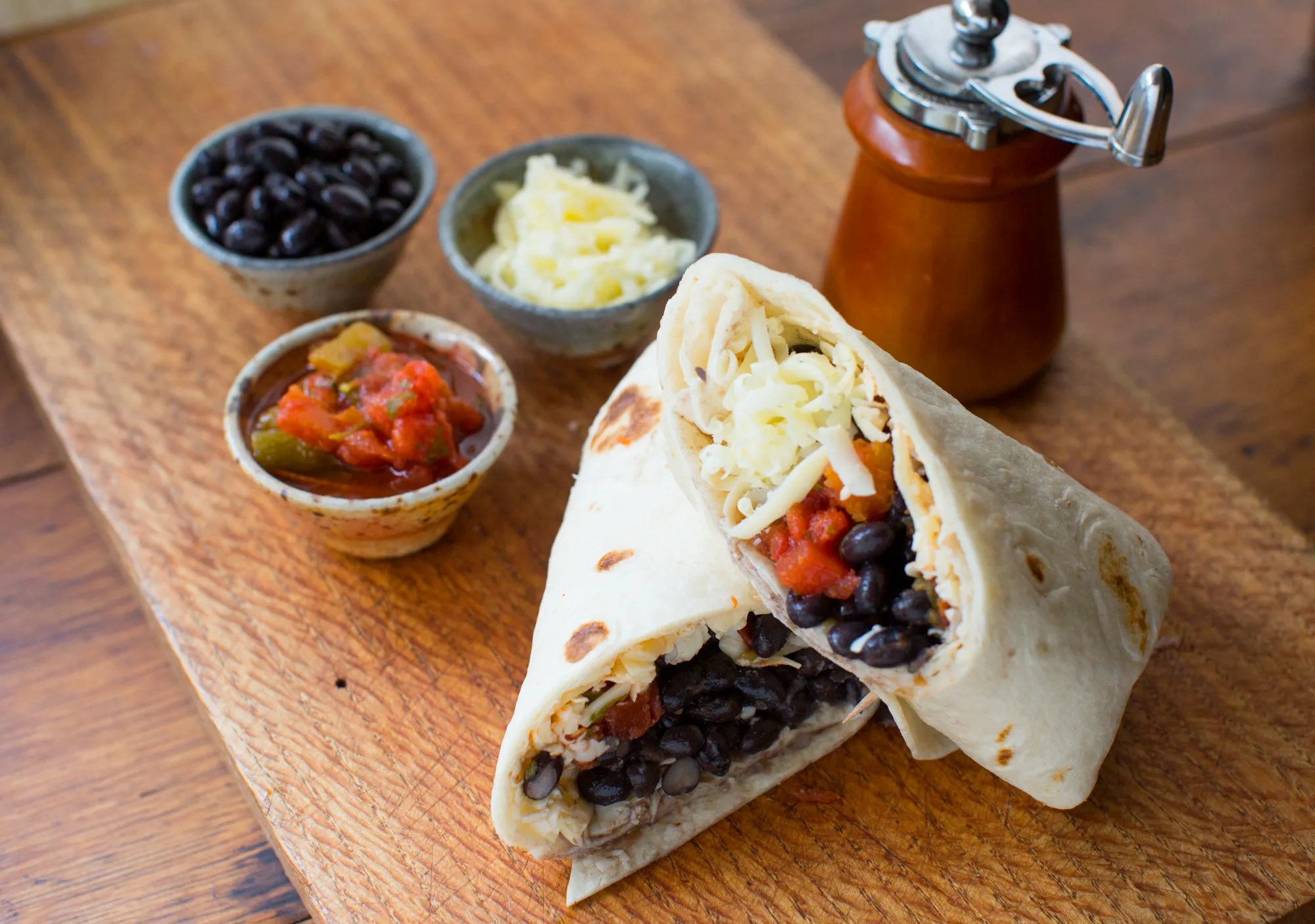 Bean burrito with black beans, salsa, cheese and pepper grinder in background