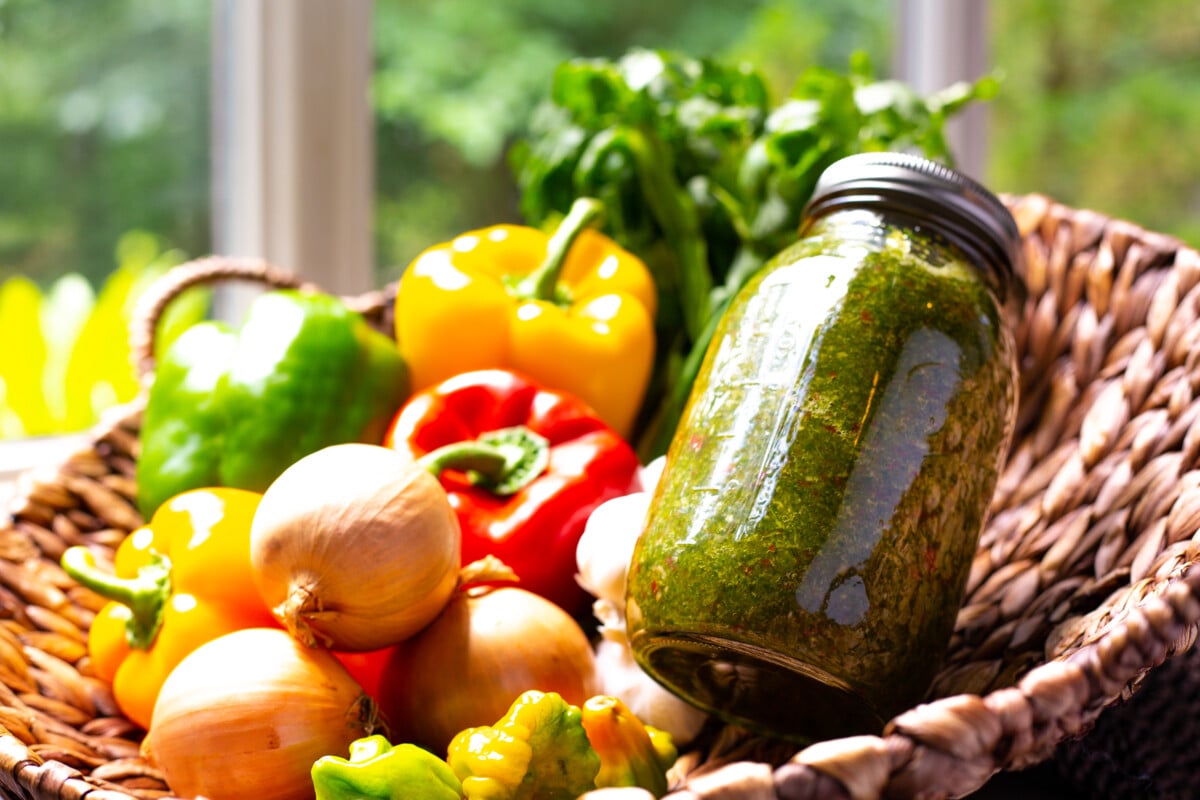 Homemade sofrito in a jar surrounded by fresh vegetable ingredients