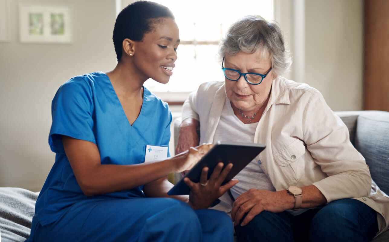 Female nurse and senior woman using a digital tablet on the sofa at home.