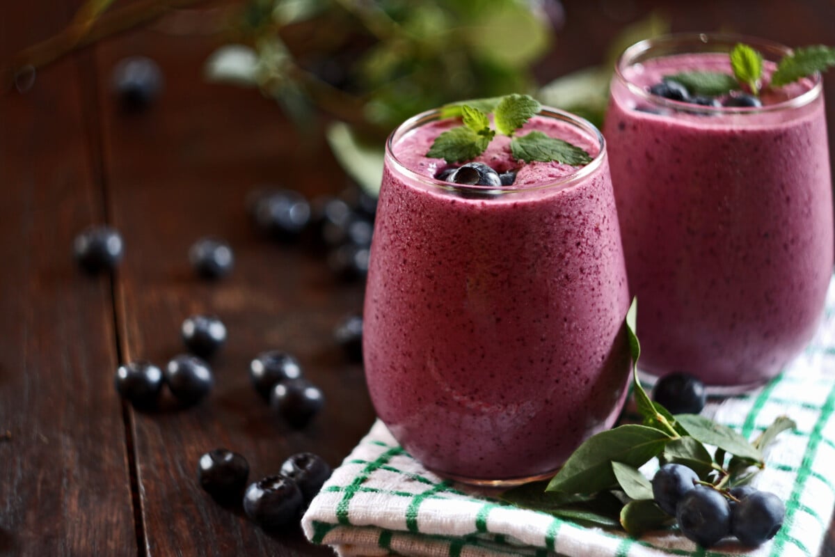 Two glasses of blueberry smoothie on a wooden table