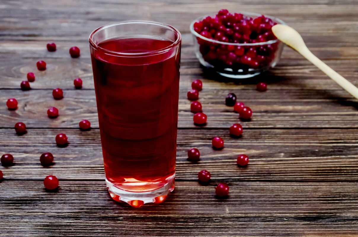 Cranberries and cranberry drink in glass on brown wooden background