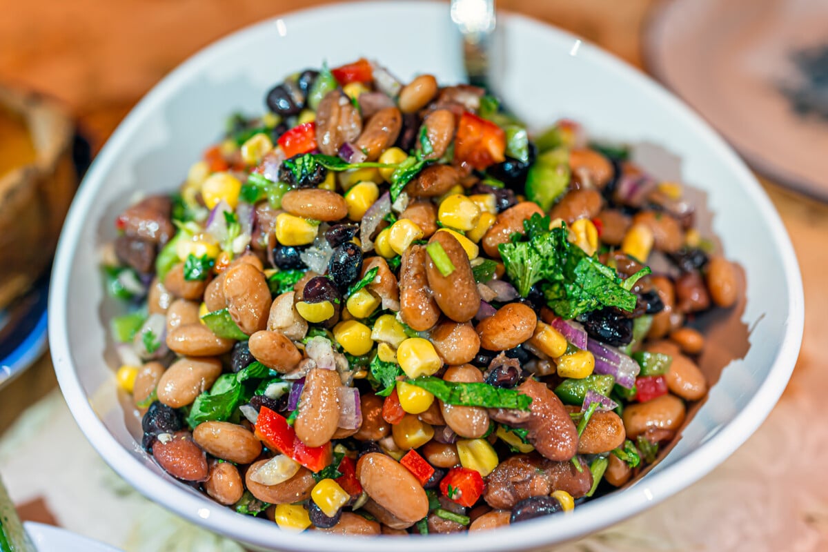 Bean salad with cilantro, red onion, raisins, peppers and corn in a white bowl