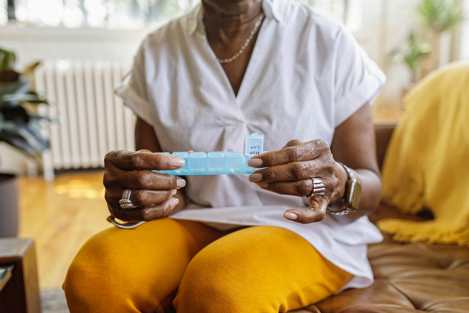 Senior woman sits on the couch at home and takes medications from a daily pill organizer.
