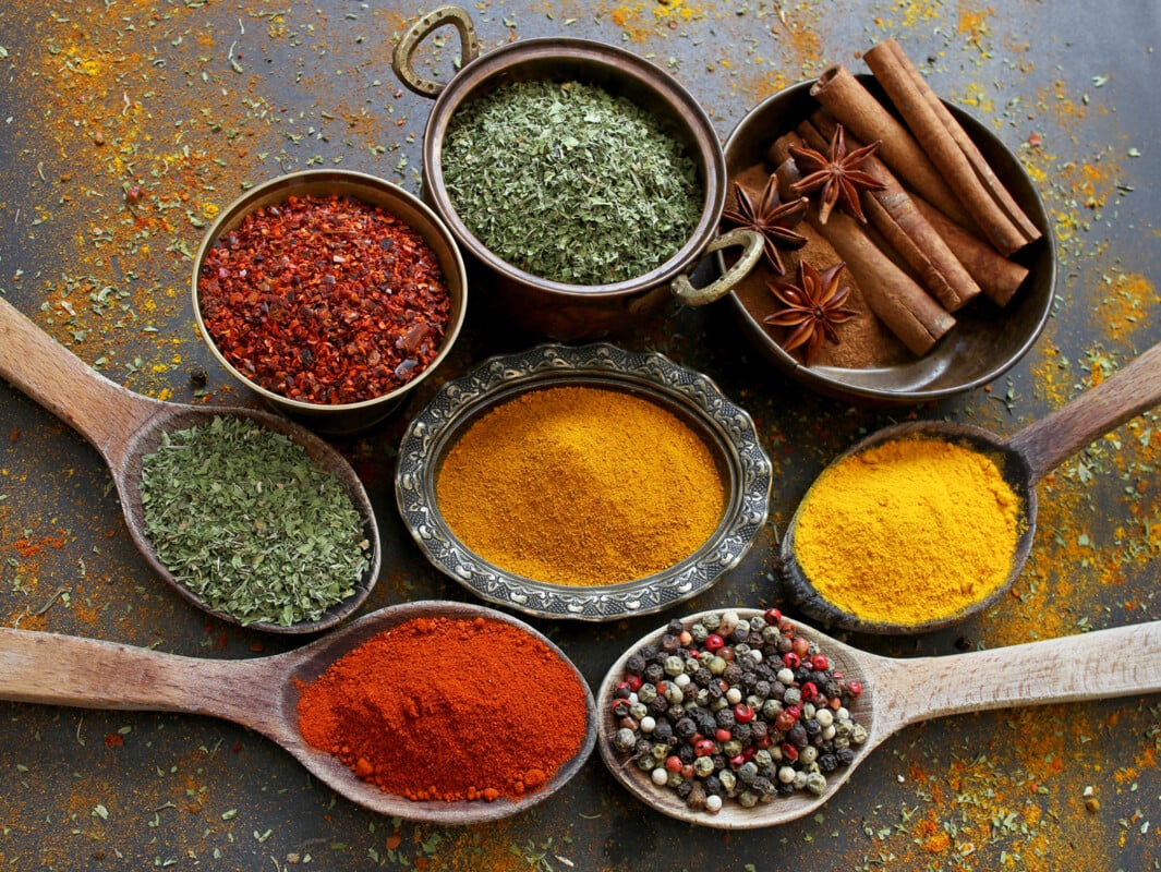 Colorful spices in various bowls and wooden spoons on black background