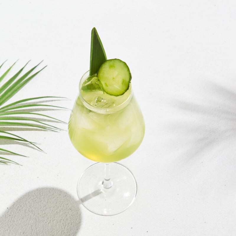 Cucumber cocktail in wine glass on white concrete background with shadows
