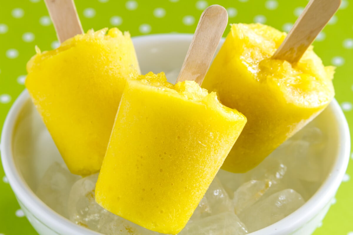 Homemade fresh pureed frozen pineapple popsicles in white bowl with ice sitting on green polka dot background
