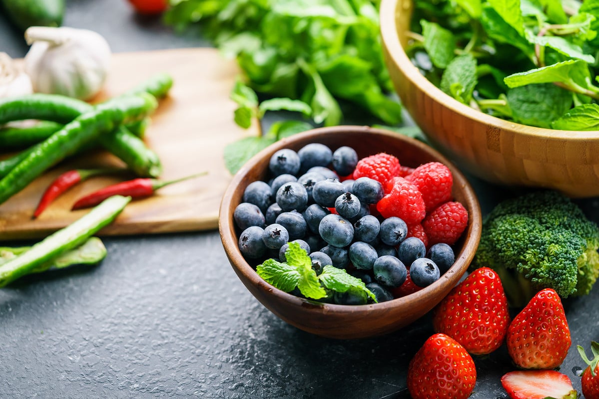 Bowl of assorted berries surrounded by leafy greens on a table