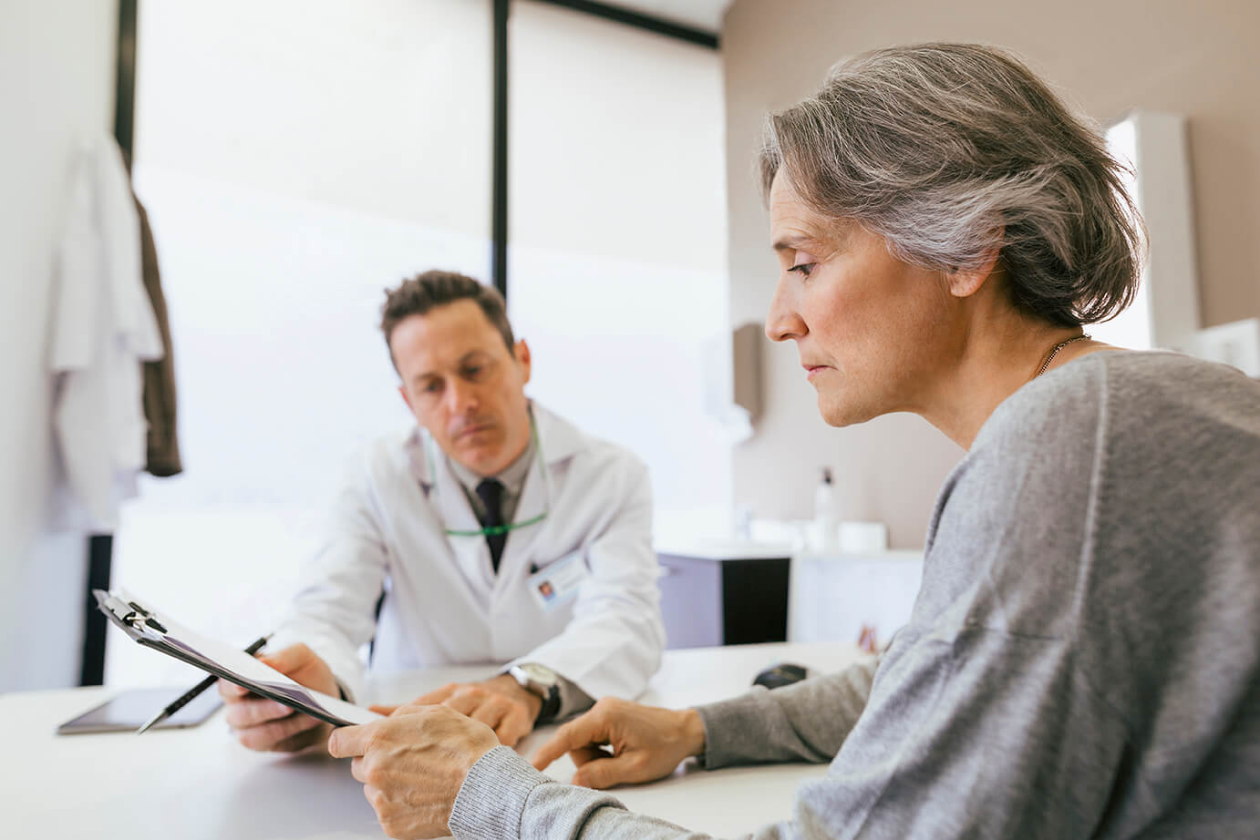 Close-up of male doctor and female patient looking at clipboard while sitting in medical clinic