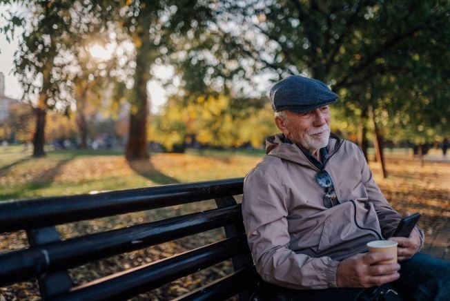 older man with coffee at the park with fall colors
