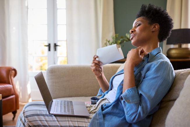 Moddle aged woman with dark skin fanning herself while working