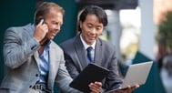 two businessmen outside using technology devices