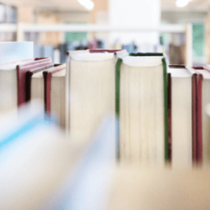 Row of hardcover books sitting on a shelf with fore-edges facing outward, set against a softly blurred library background.