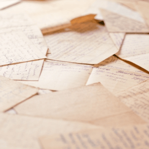 Scattered vintage handwritten letters and notes with cursive ink script resting on aged, beige-toned paper.