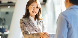 A smiling businesswoman shaking hands with someone in an office setting.