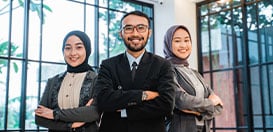 Three smiling business professionals standing together with their arms crossed.