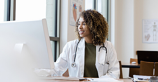 COVID-19 Forcing Healthcare Providers to Rethink Just-in-Time Supply Chain Management- A smiling doctor looking at her laptop