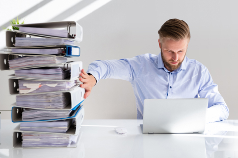 man pushing away physical stack of binders in favor for laptop