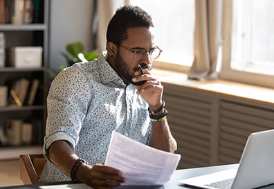 Man working in his office holding papers on his hand and looking at his laptop
