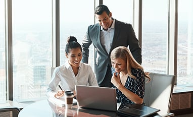 A man and two women in an office looking at a laptop on a desk