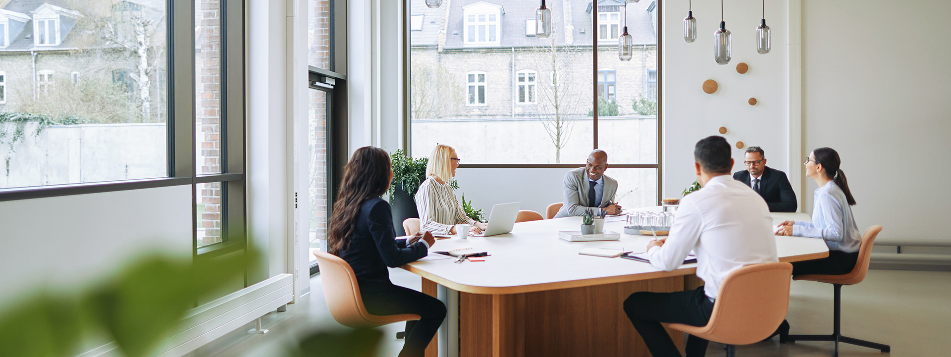 six people inside an office space with a lot of natural lighting, conducting a meeting