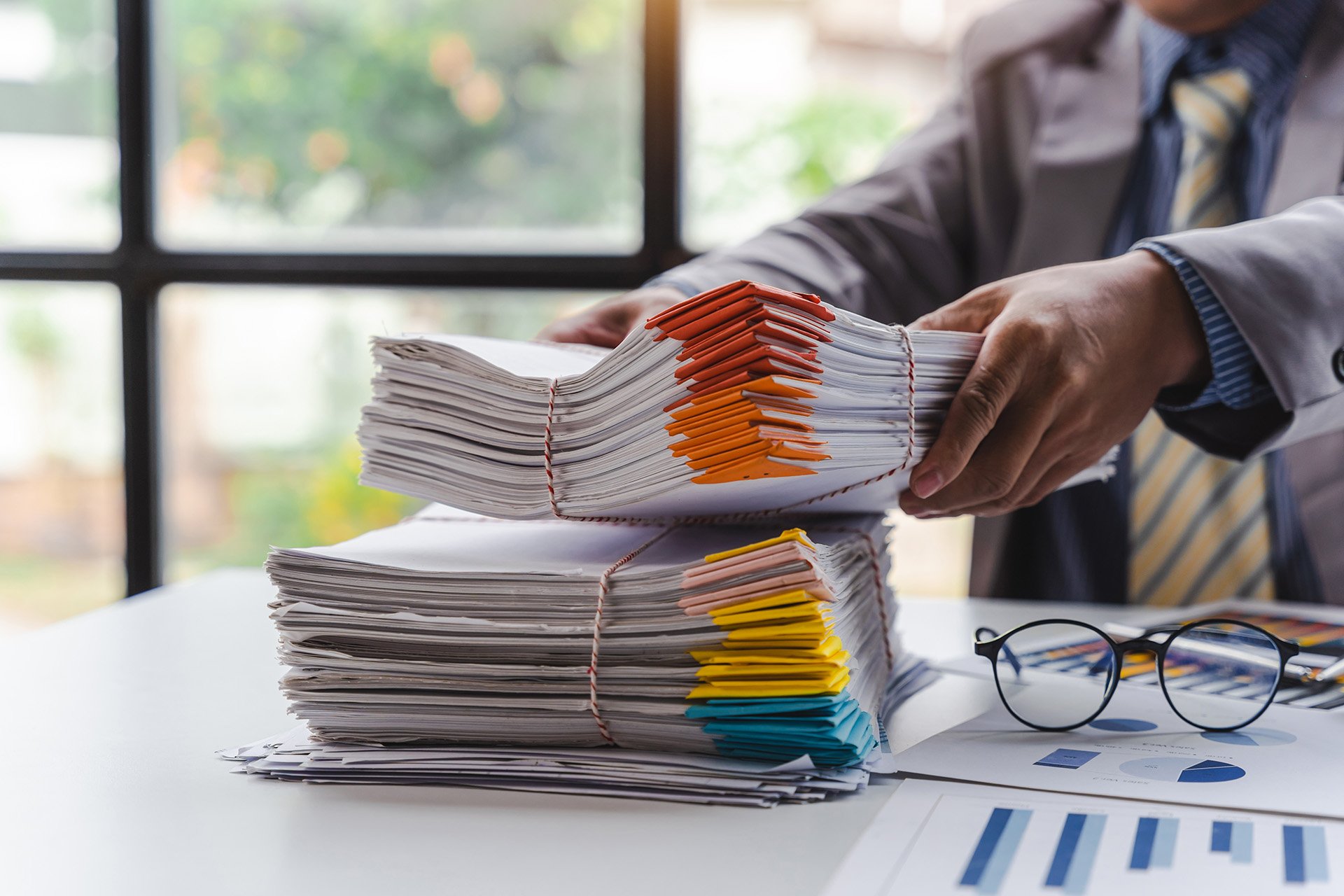 businessman picking up bundle of files off of desk