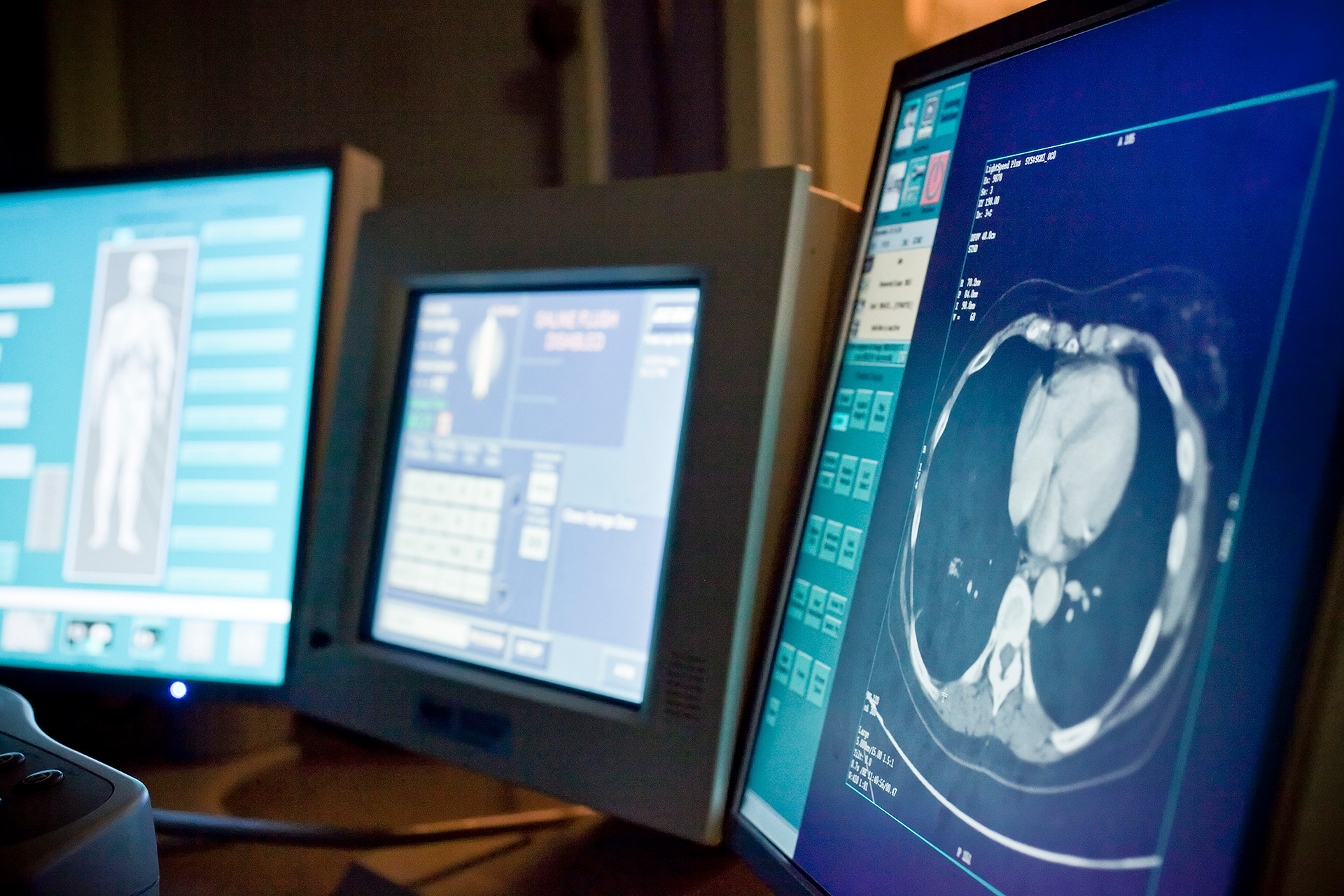 three computers in dimly lit room displaying healthcare information