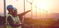 two energy workers pointing at windmills during sunset