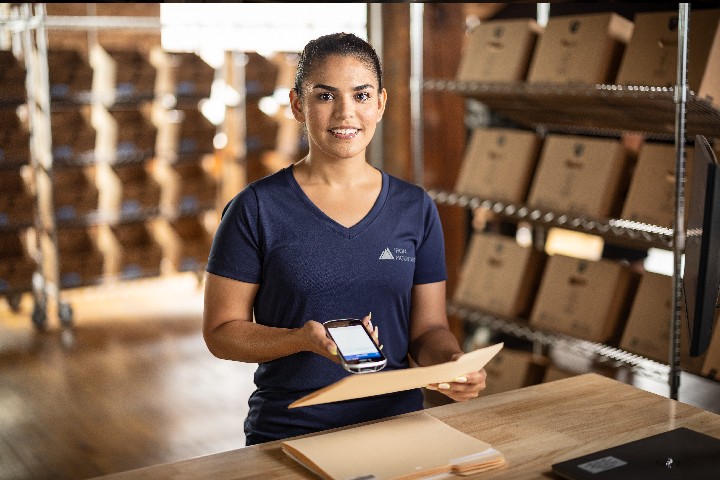 IM employee holding mobile scanner, with IM warehouse backdrop