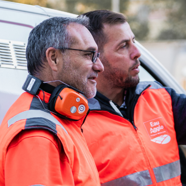 Two field technicians in high-visibility orange workwear standing beside a service vehicle, discussing utility network operations.