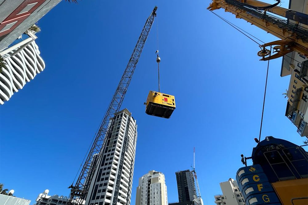 A large generator unit being crane lifted over a construction site