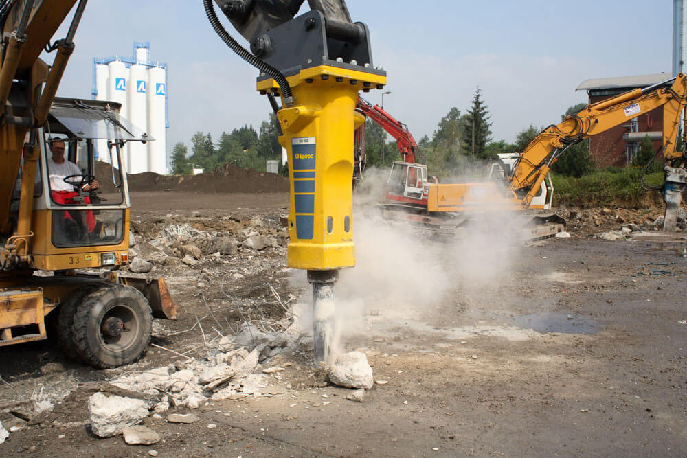 An excavator with a breaker attachment breaking concrete