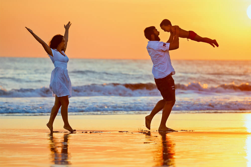 A couple and a kid walking on a beach at sunset