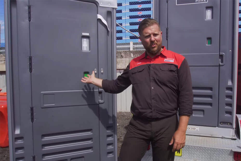 Kennards Hire team member pointing at a portable toilet