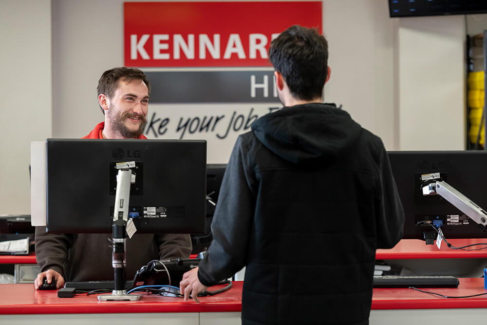 A customers back facing to the camera, speaking to a Kennards Hire team member over the branch service desk