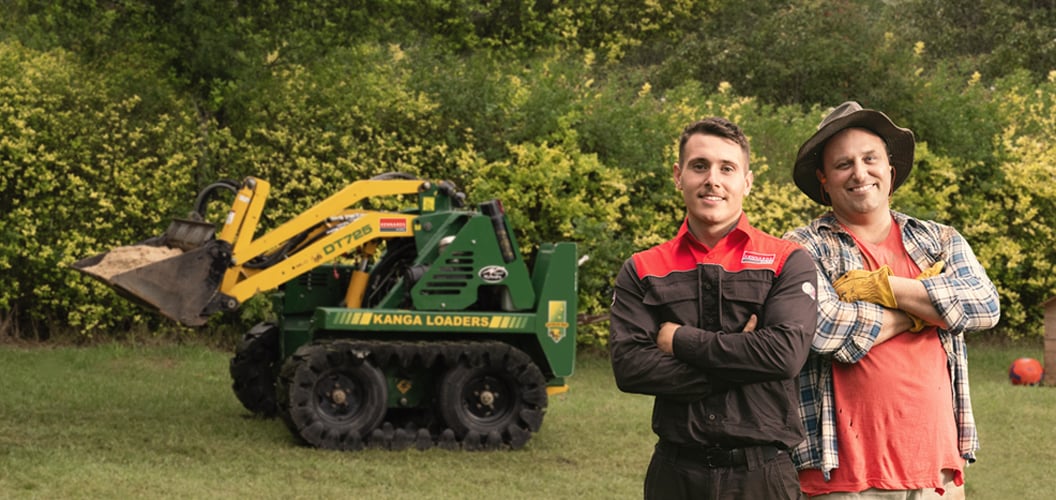 Kennards Hire team member standing next to a DIYer and  a mini loader in a backyard 
