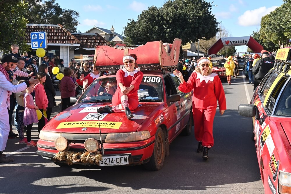 two people dressed up in red costumes with a red rally car