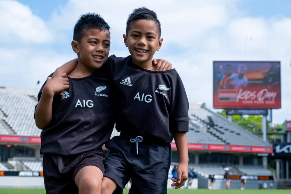 Two boys wearing All Blacks jerseys arms over shoulders at Eden Park Stadium