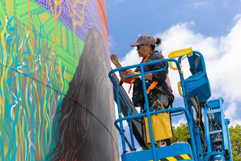 An artist riding a boomlift painting on a silo