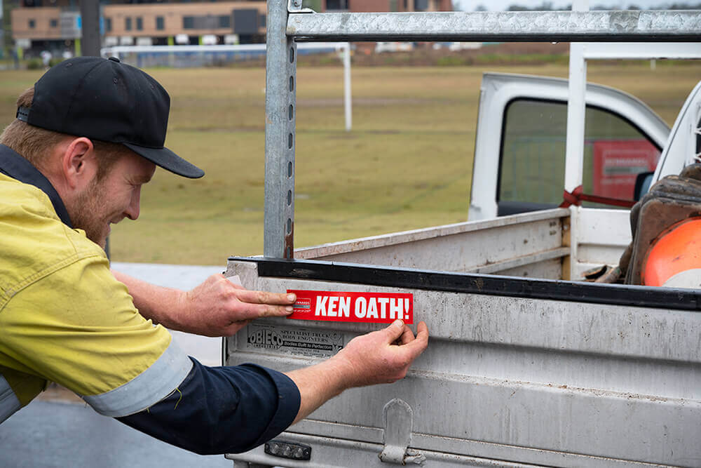 Tradie putting a ken oath sticker on his ute