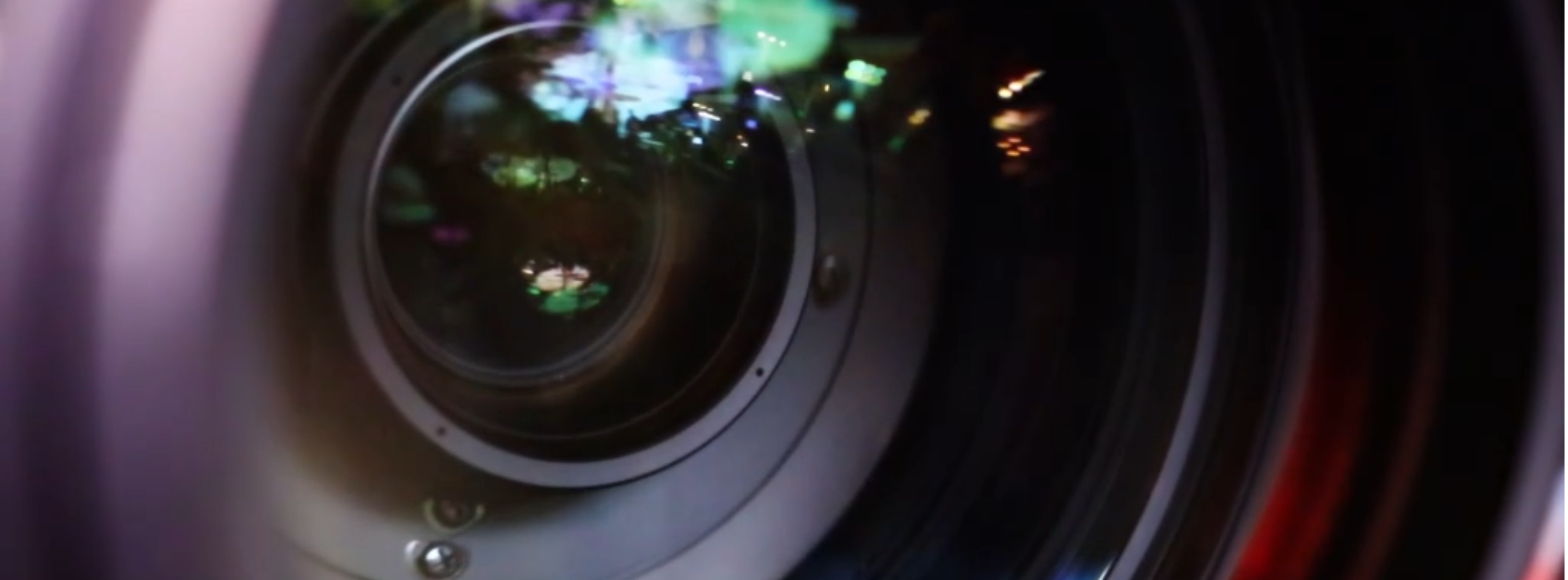 Close up of a dark camera lens, the lens is reflecting vibrant green and purples